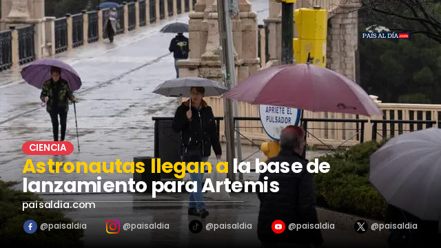 Astronautas con trajes espaciales en la base de lanzamiento, rodeados de equipos de apoyo y vehículos espaciales.