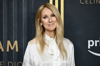 Céline Dion sonríe en el escenario, luces brillantes y público emocionado al fondo.