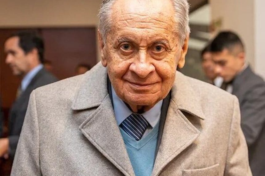 Marco Fidel Rocha en su oficina, rodeado de libros y diplomas, mirando hacia la ventana con una expresión reflexiva.