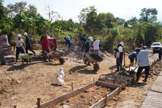 Grupo de jóvenes indígenas trabajando en la construcción de una vía rural en Paniquita bajo un cielo despejado.