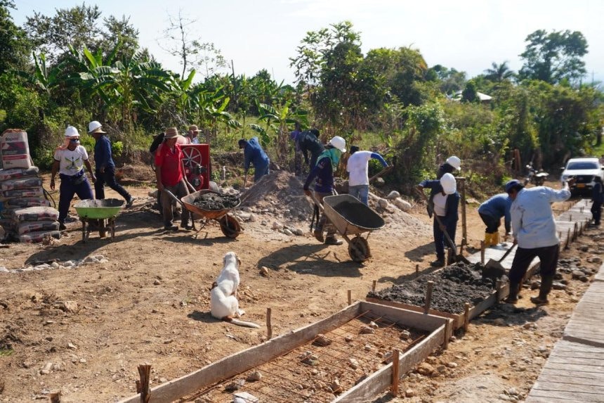 Grupo de jóvenes indígenas trabajando en la construcción de una vía rural en Paniquita bajo un cielo despejado.