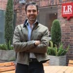 Una mujer sonriente revisa su celular en una cafetería, con un logo de Addi visible en la mesa.