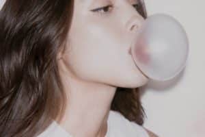 Olivia Rodrigo en un fondo colorido, con mirada intensa y atuendo moderno, mientras sostiene un micrófono.