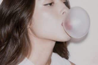 Olivia Rodrigo en un fondo colorido, con mirada intensa y atuendo moderno, mientras sostiene un micrófono.