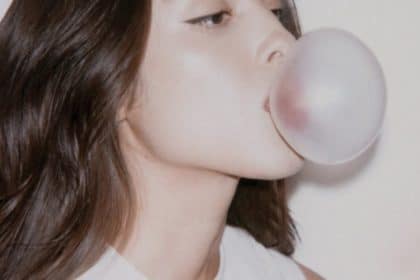 Olivia Rodrigo en un fondo colorido, con mirada intensa y atuendo moderno, mientras sostiene un micrófono.