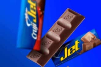 Un grupo de jóvenes sonrientes sostiene chocolatinas Jet en un parque, disfrutando de un día soleado.